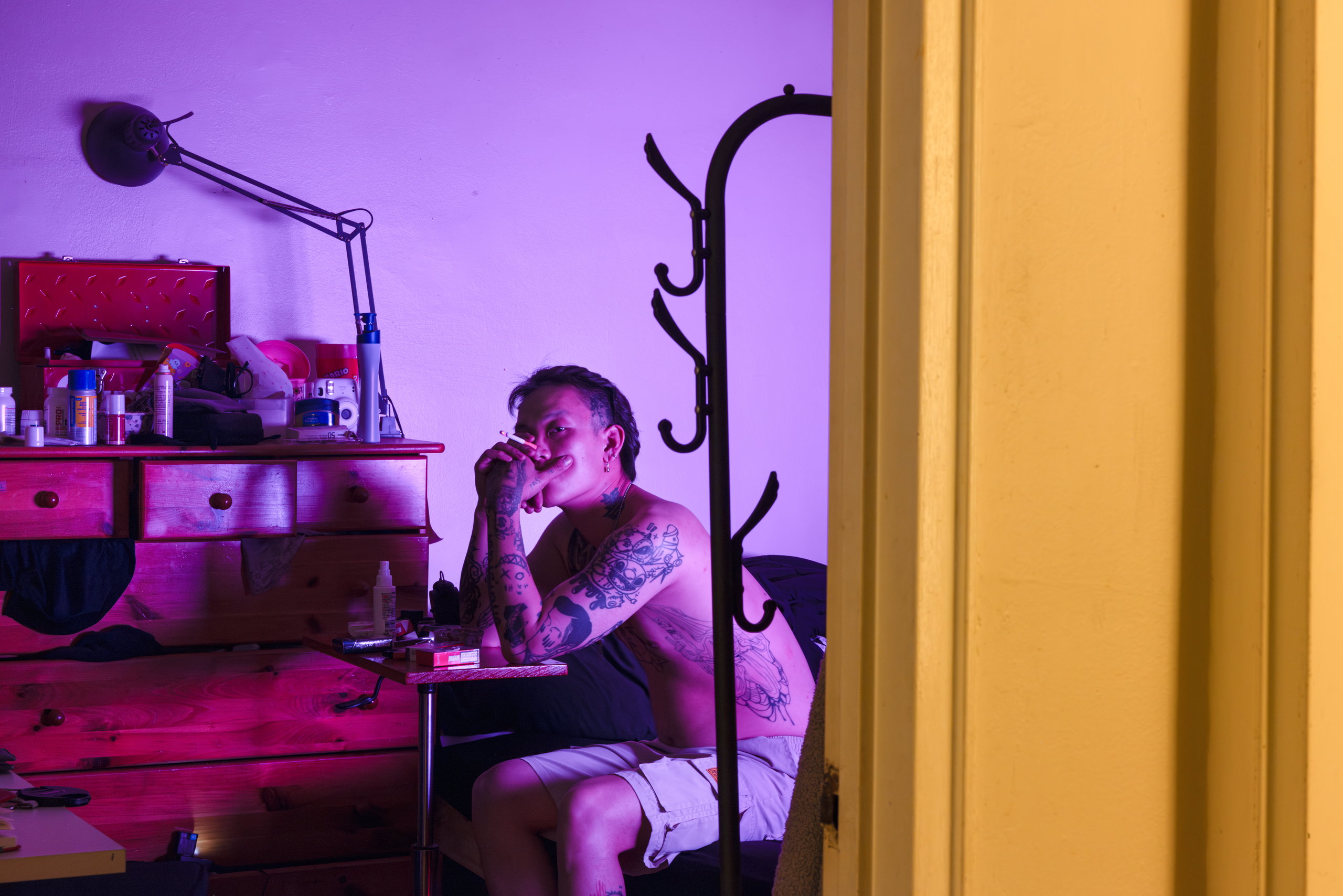 Seen through a doorway, a man sits in a cluttered room lit in purple and red — Win or Lose