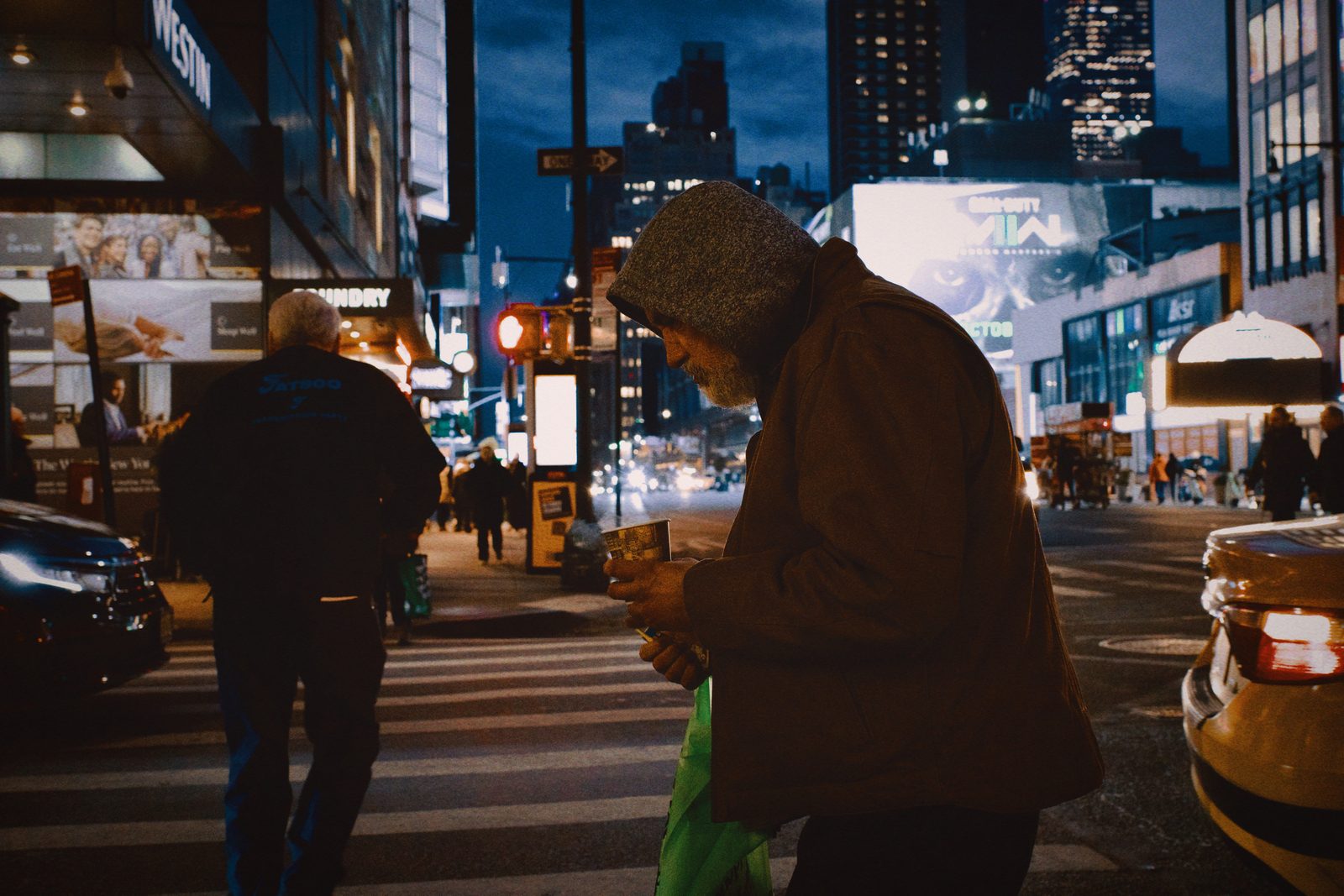 A crowd crossing the street at night, billboards above — New York
