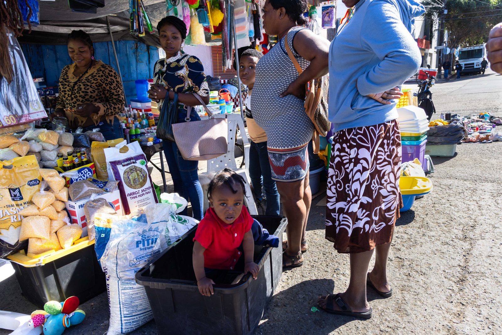 A crowded market, a girl in a red top seated among stalls and shoppers — The Liminal Innocence