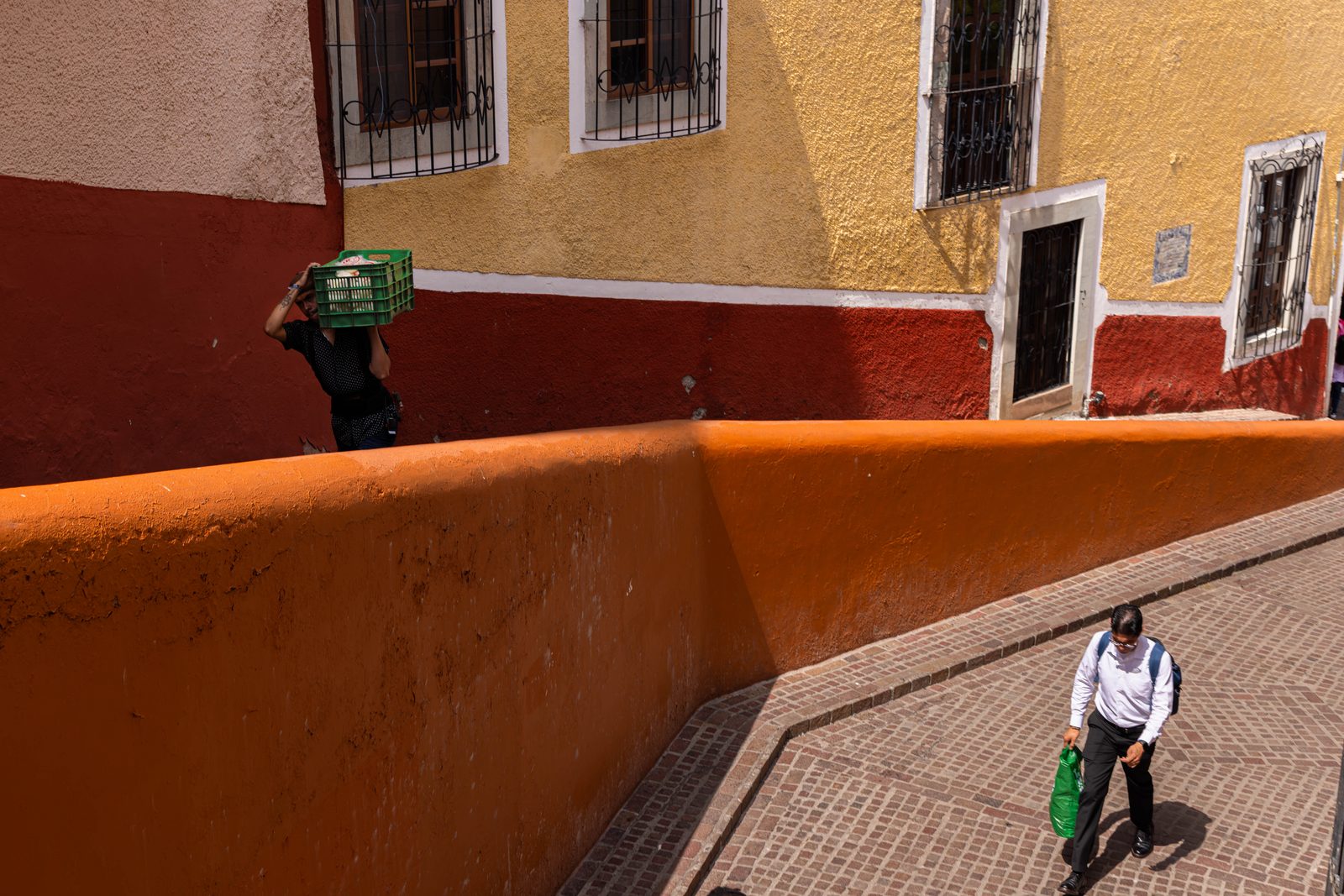 Looking down on a street corner, a small child walks below an orange wall — The Liminal Innocence