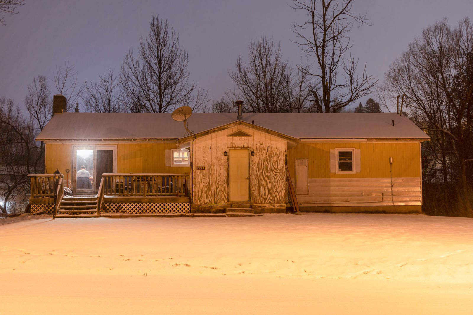 A small house lit warm against snow at dusk — Lake Placid