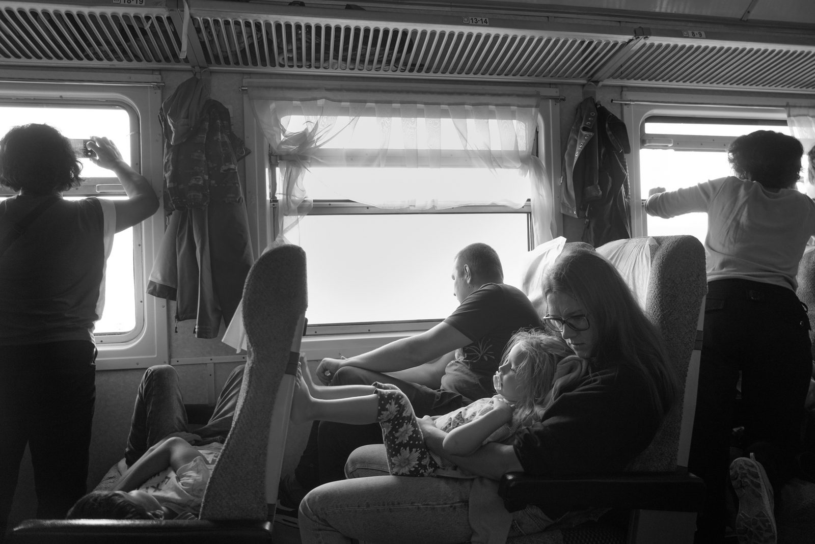 Black-and-white interior of a train carriage, passengers resting as bright light pours through the windows — Lake Baikal